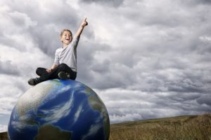 A boy sits on top of a globe with a dramatic landscape in the background.Click on an